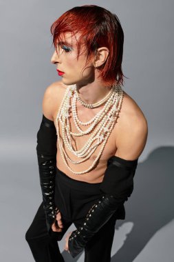 Çarpıcı genç adam, çağdaş bir stüdyoda sanatsal stil ve katmanlı aksesuarlar sergiliyor..