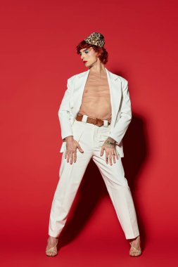 Cesur beyaz bir takım elbise giyen bu genç adam kendine güvenerek duruyor ve eşsiz bir stil sergiliyor..