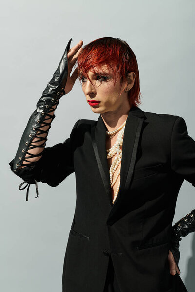 Молодой человек стилизует свои яркие волосы, надевая элегантный, но резкий наряд, источая уверенность.