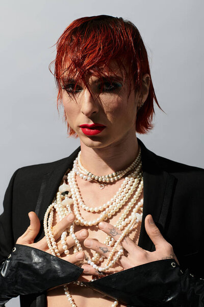 Молодой человек демонстрирует творческий выбор моды, украшенный жемчугом и ярким макияжем.