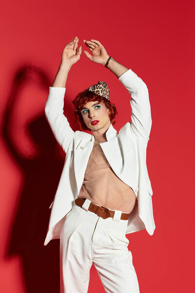 With a striking pose and expressive style, a young man showcases bold fashion against vivid red.