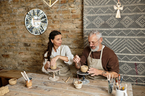 A mature couple enjoys quality time together in a pottery class, shaping clay.