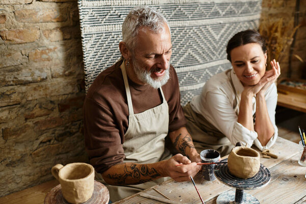Mature couple enjoys shaping clay in a pottery class, sharing laughter and creativity.