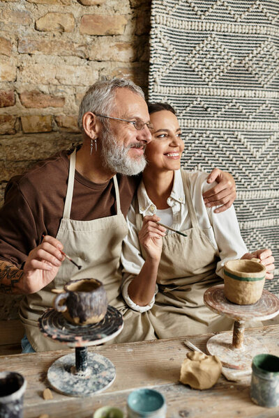 A beautiful couple molds clay in a pottery class, sharing smiles and quality time together.