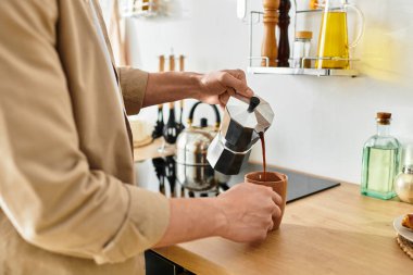 A young man in casual clothes pours coffee into a mug, savoring the morning at home. clipart