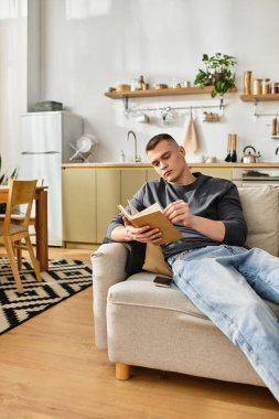 Casually dressed young man enjoys an afternoon reading in his stylish apartment space. clipart