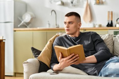 Genç bir adam şık bir dairede rahatlar, rahatça kitap okur..