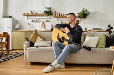 Genç bir adam, rahat ve şık dairesinde gitar tıngırdatarak kanepede dinleniyor..