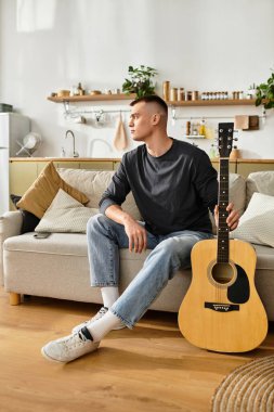 Genç bir adam şık dairesinde bir kanepede oturur, gitar tutar ve müzik dinler..