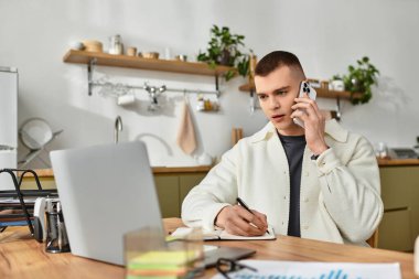 Yakışıklı genç bir adam masasında notlar alırken bir telefon görüşmesi yapıyor..