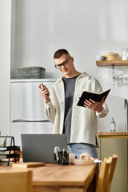 Sıradan giyinmiş genç bir adam evde çalışırken bilgisayarına odaklanmış vazifelerini dengeliyor..