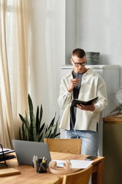 Gündüz kıyafetli genç adam güneşli bir dairede dikilirken notlar çalışıyor..