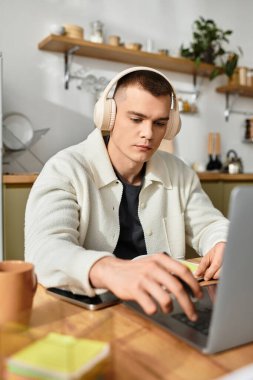 Gündelik kıyafetleri olan genç adam, şık, ahşap bir masada otururken dizüstü bilgisayarında yazı yazıyor..