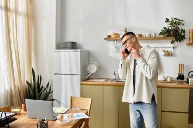 Gündelik giyinmiş genç bir adam, modern dairesinden çalışırken bir telefon görüşmesi yapıyor..