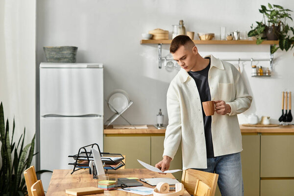 A focused young man works at home, sipping coffee while organizing documents in a relaxed setting.