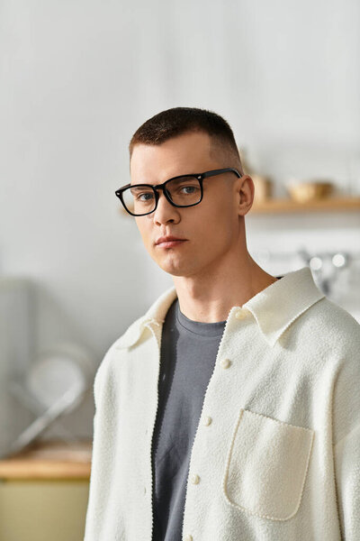 A young man in casual attire and glasses in a modern apartment.