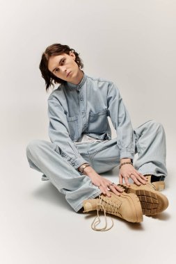 Yakışıklı genç bir adam yerde oturuyor, kot giyip, benzersiz tarzını sergiliyor..