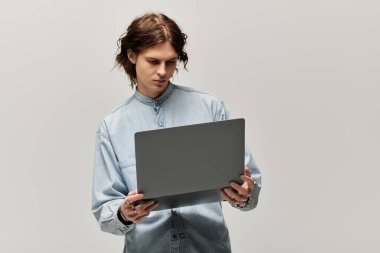 Kot gömlek giyen yakışıklı genç bir adam minimalist bir ortamda dizüstü bilgisayarı inceliyor..