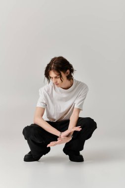 Genç bir adam şık bir kıyafet içinde şık bir şekilde çömeliyor, sanatsal cazibesini açık bir ortamda gösteriyor..