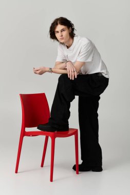 A handsome young man showcases his unique fashion style while leaning on a vibrant red chair. clipart