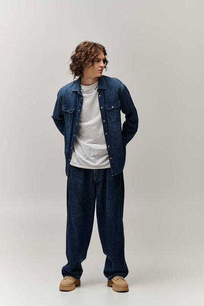 Красивый молодой человек уверенно стоит, одетый в повседневный, но модный наряд.