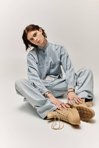 Красивый молодой человек сидит на полу в джинсовом ансамбле, демонстрируя свой неповторимый стиль..