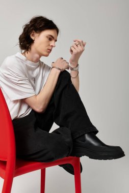 Moda kıyafetli yakışıklı bir genç adam düşünceli bir şekilde otururken eşsiz tarzını sergiliyor..