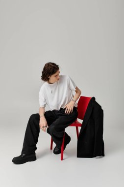 Yakışıklı genç adam yaratıcı bir stüdyo ortamında kırmızı bir sandalyede rahat eder..