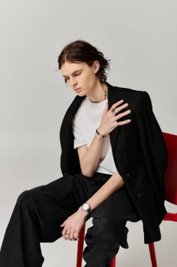 Şık giyinmiş yakışıklı bir genç adam düşünceli bir şekilde parlak kırmızı bir sandalyeye oturur..