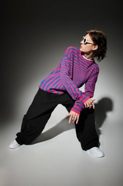 Şık bir genç adam dinamik bir poz verir, kalın çizgiler ve şık güneş gözlüğü takar..