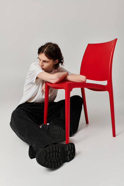Красивый молодой человек в повседневной одежде игриво соединяется с ярко-красным стулом в помещении.