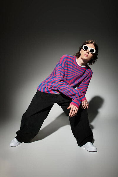 Стильный молодой человек уверенно позирует в ярком полосатом свитере и свободных брюках.