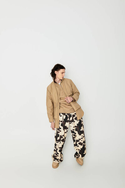 Молодой человек демонстрирует современный стиль с уникальным выбором одежды в гладкой студии.