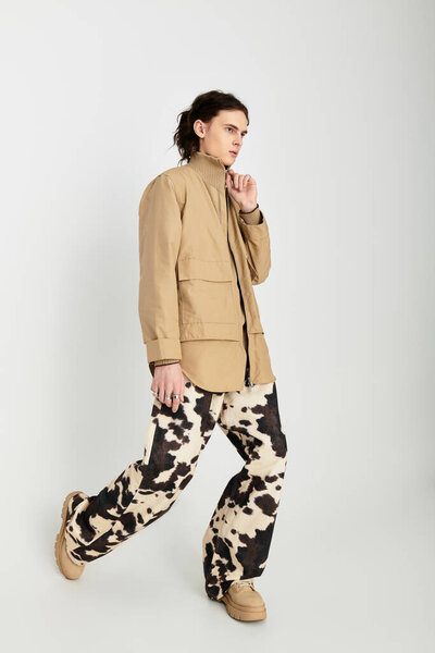 A handsome young man poses confidently in a neutral toned outfit with bold designs, exuding style.