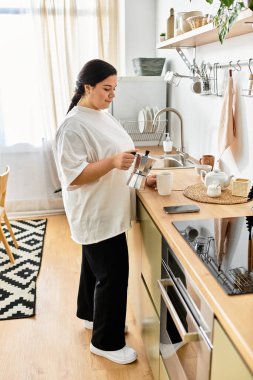 Bright light floods a cozy kitchen as a young plus sized woman prepares coffee with a smile. clipart