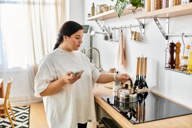 Parlak mutfak, doğal ışıkla yıkandı. Gülümseyen, kilolu bir kadın yemek pişiriyor..