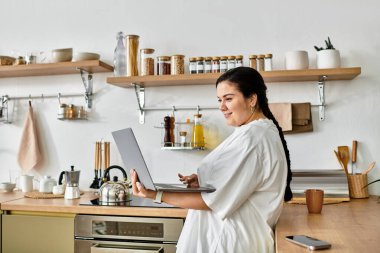 Parlak ve davetkar bir mutfak. Bir kadın dizüstü bilgisayarıyla uğraşırken, gülümsüyor..