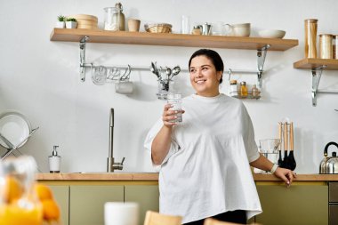Genç bir kadın, elinde bir bardak ferahlatıcı suyla şık bir mutfakta gülümsüyor..