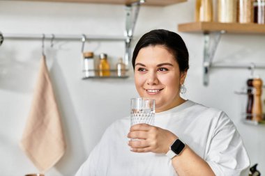 Parlak ve neşeli genç bayan elinde bir bardak su tutuyor, şık mutfağında gülümsüyor..