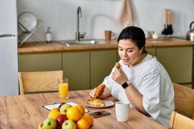 A young plus sized woman savors pastries and fresh fruit, relishing her breakfast moment. clipart