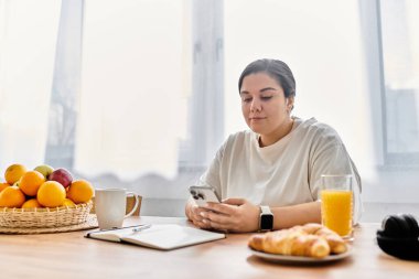 Genç ve iri yarı bir kadın sabah kahvaltısında telefonuna bakar..