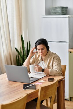 Odaklanmış genç bir kadın, bilgisayarını parlak, rahat bir mutfak düzeninde kurarken kahvenin tadını çıkarıyor.