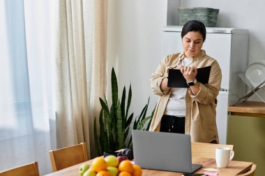 Parlak bir mutfakta, genç ve iri yarı bir kadın tabletiyle etkileşime girer. Meyvelerle çevrilidir..