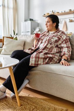 A beautiful plus sized woman savors her drink while lounging comfortably in a cozy living room. clipart