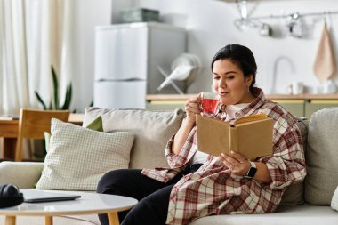 Genç, iri yarı bir kadın kanepede rahatlar, çayını yudumlar ve kitap okur..
