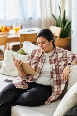 Parlak bir oturma odasında dinlenen, güzel, iri yarı bir kadın, huzur saçan bir kitap okuyor..