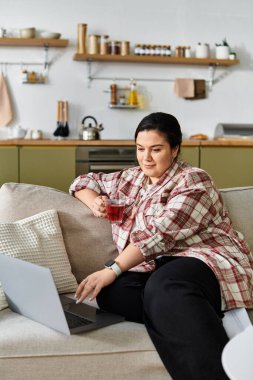 Cozy afternoon with a young plus sized woman sipping tea and engrossed in her laptop work clipart