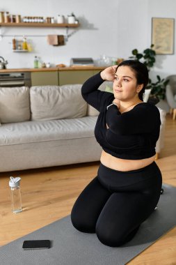 Yoga minderinin üzerinde diz çökmüş genç ve güzel bir kadın evindeki sağlık yolculuğunu yansıtıyor..