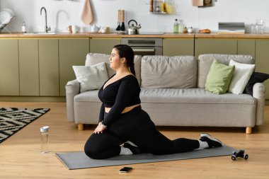 Genç ve iri yarı bir kadın şık, rahat oturma odasında yoga minderinin üzerinde zarifçe uzanır..