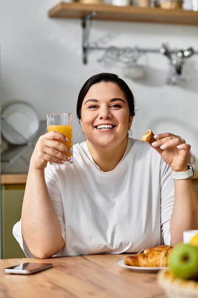 Savoring a beautiful morning, a young plus sized woman enjoys a croissant and fresh juice with joy.